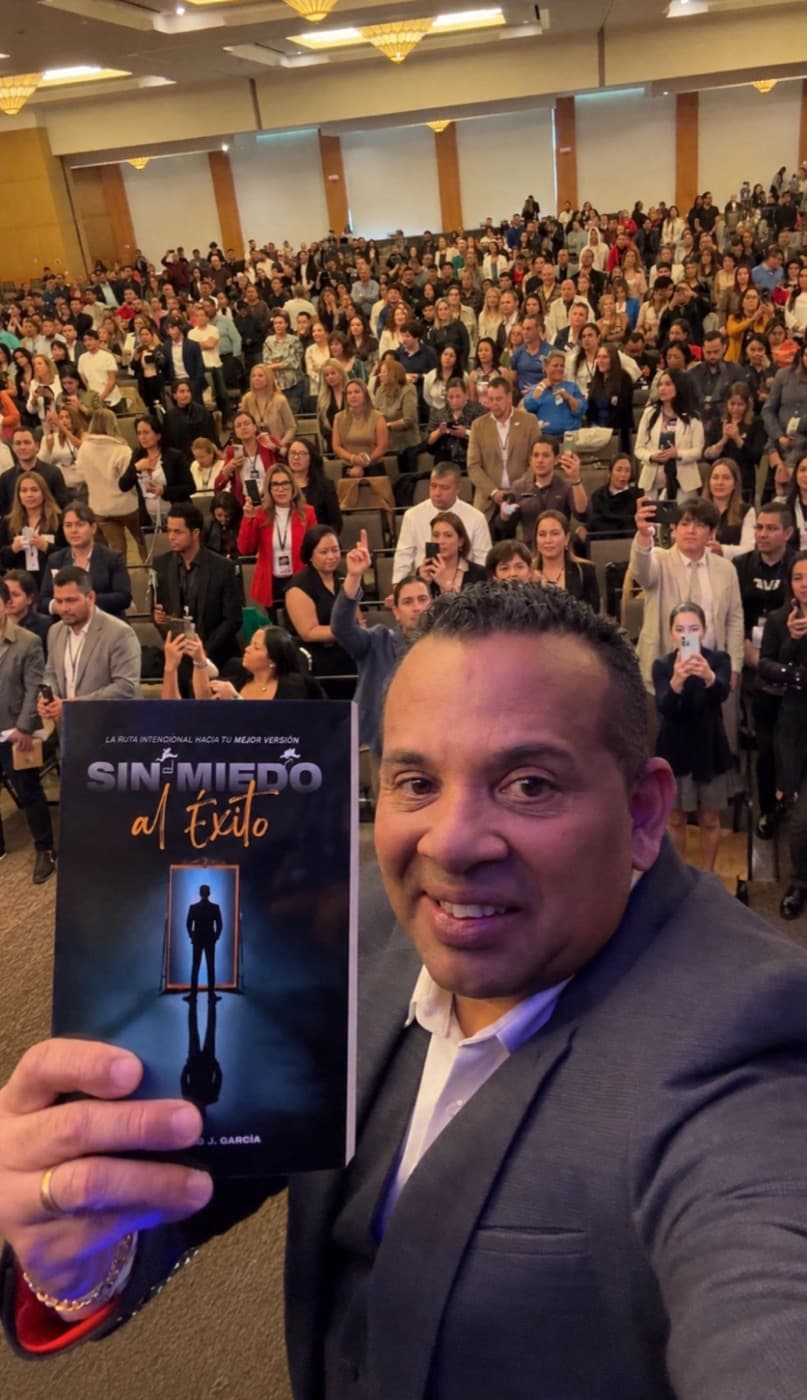 Jairo J. García sosteniendo su libro Sin Miedo al Éxito frente a un auditorio lleno de cientos de asistentes